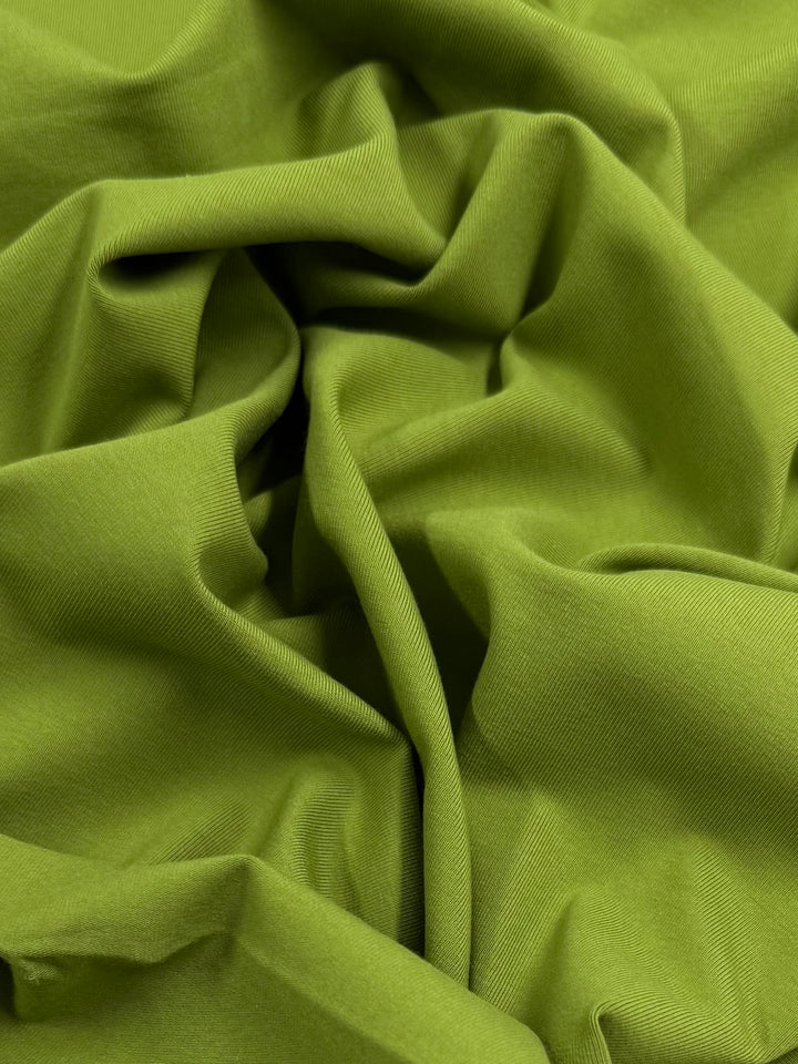 A close-up of crumpled, soft Cotton Lycra - Spinach Green from Super Cheap Fabrics shows gentle folds and smooth, stretchy texture with a slight sheen in soft light—ideal for crafting bodycon dresses that fit perfectly. Width: 167cm.