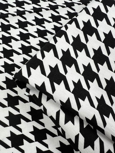 Close-up of Super Cheap Fabrics' Printed Bengaline - Grande Houndstooth (150cm). The black and white geometric shapes align closely, with one piece folded over another, highlighting the textured look of this medium-weight fabric.