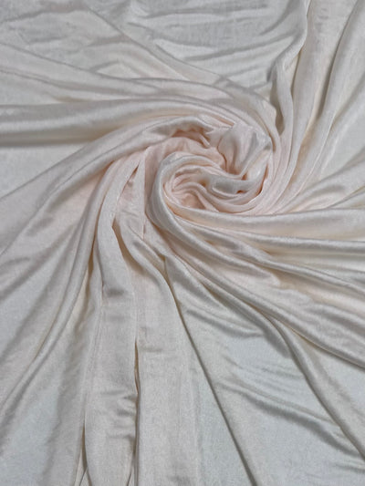 The Knit Lining Shimmy by Super Cheap Fabrics in cream features pale pink polyester artistically swirled at the center, forming a spiral pattern. Its lightweight, soft texture and subtle sheen capture the light beautifully. Width: 130cm.