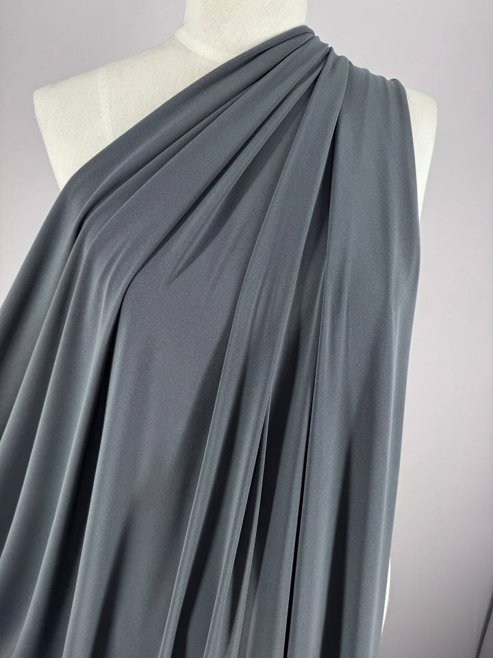 The Super Cheap Fabrics ITY Knit - Charcoal - 150cm is draped over a mannequin's shoulder, showcasing its soft, flowing folds and elegant twist yarn texture against a plain light background.