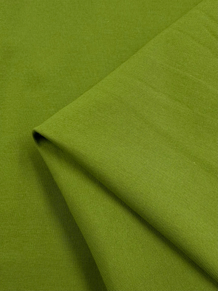 Close-up of a folded piece of vibrant Cotton Lycra - Spinach Green by Super Cheap Fabrics, highlighting its smooth texture and diagonal seam. The rich color and weave pattern, typical of bodycon dresses, add depth.