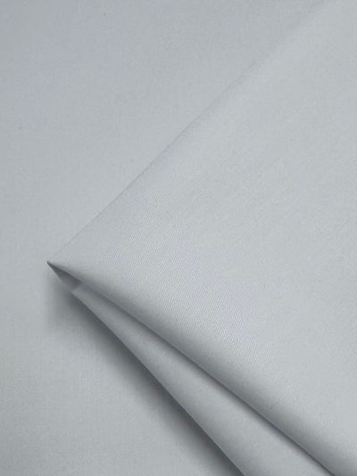 A neatly folded piece of white gabardine fabric from Super Cheap Fabrics, measuring 150cm, lies on a flat surface with its smooth and wrinkle-resistant texture featuring subtle diagonal lines.