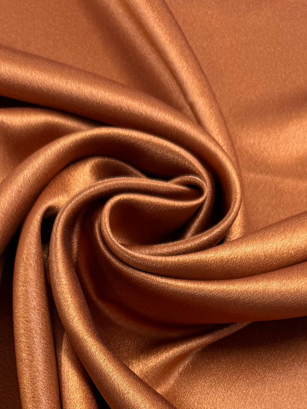 Satin Back Crepe - Desert Sun by Super Cheap Fabrics features glossy, coppery folds that form a spiral pattern, making this 150cm wide fabric ideal for elegant tops or luxurious eveningwear.
