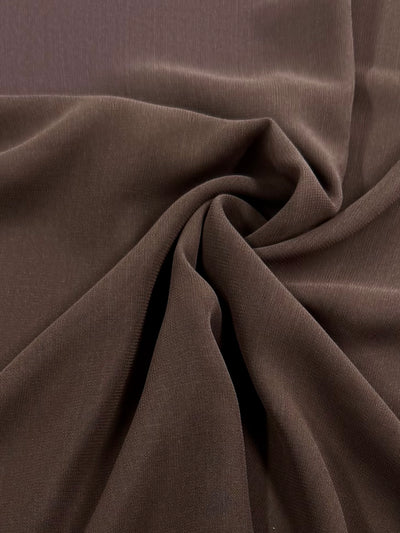 Close-up of the Super Cheap Fabrics Hi-Multi Chiffon in Potting Soil, showcasing its dark brown polyester with a soft, velvety texture. Gathered in the center with lighting that highlights its smooth, rich feel and lightweight nature. Width: 150cm.