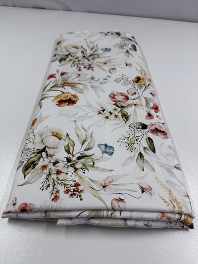 A folded piece of Super Cheap Fabrics' Cotton Sateen - 180cm rests on a white surface, measuring 125cm by 180cm. It features an elegant floral pattern with pink, yellow, and green flowers and delicate leaves for a natural look.