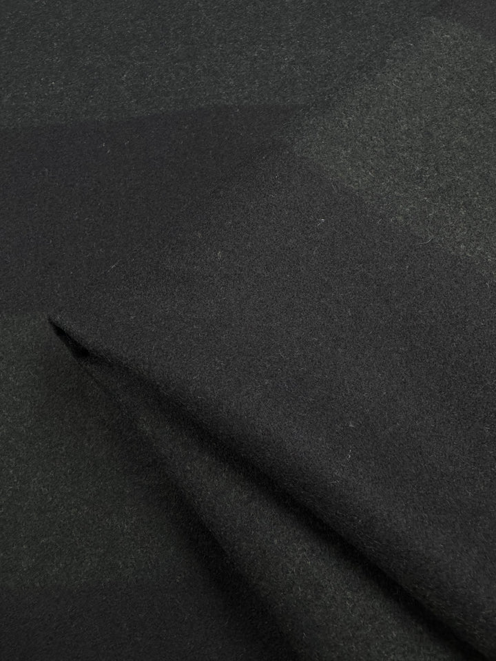 Close-up of Super Cheap Fabrics' Virgin Wool in a two-tone black khaki pattern. The soft, heavy weight wool displays a subtle plaid design, with gentle folds emphasizing its texture and weave. Width: 150cm.