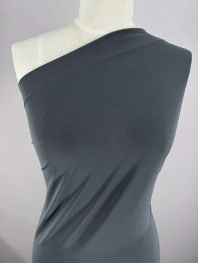 A white mannequin showcases a dark gray, one-shoulder garment made from Super Cheap Fabrics’ ITY Knit - Charcoal (150cm), draped diagonally across the torso and displayed against a plain light background.