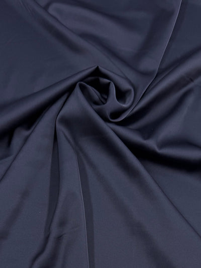 Silky Satin - Navy - 150cm by Super Cheap Fabrics features a smooth, dark navy blue surface with gentle folds and soft shadows created by loosely gathered fabric.
