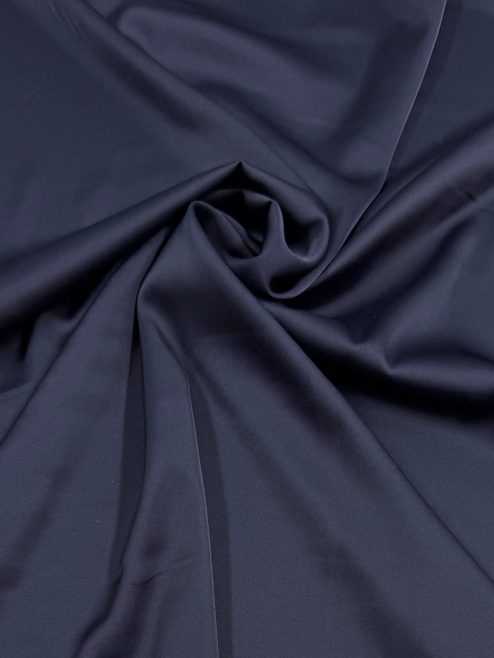 Silky Satin - Navy - 150cm by Super Cheap Fabrics features a smooth, dark navy blue surface with gentle folds and soft shadows created by loosely gathered fabric.