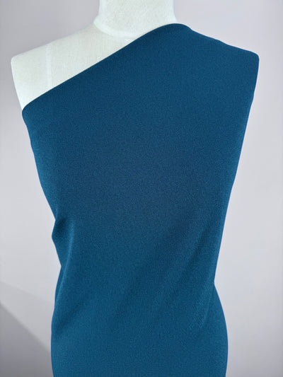 A mannequin showcases Super Cheap Fabrics' Plain Crepe - Teal (150cm), a textured, medium-weight fabric with a one-shoulder design, set against a plain light background.