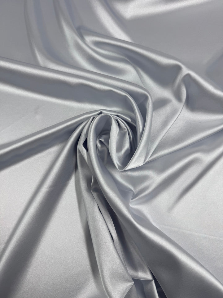 The Stretch Satin Deluxe - Silver - 150cm by Super Cheap Fabrics features smooth, shiny silver satin that's artfully gathered and twisted at the center, creating elegant folds and soft textures on this lightweight fabric.