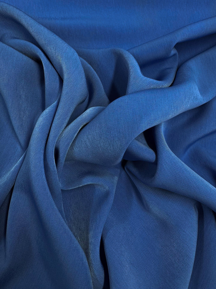 A close-up of crumpled, smooth Microfibre Suiting fabric by Super Cheap Fabrics in Bright Cobalt, highlighting its soft texture and rich color variations from light to dark blue within the folds.