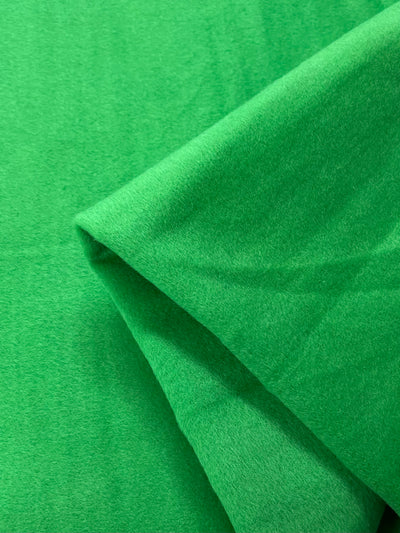 Close-up of the Titanite Wool Cashmere fabric by Super Cheap Fabrics. This vibrant green material, 150cm wide, showcases its plush texture and flexibility through soft folds, smooth lines, and subtle shadows.
