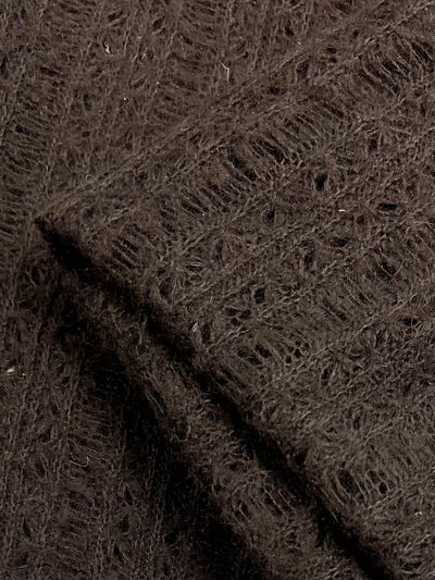 Close-up of Super Cheap Fabrics' Wool Knit in Dark Chocolate (140cm), featuring a textured, open-weave pattern with small gaps and a slightly fuzzy, soft surface. The lightweight fabric shows visible fibers and a layered appearance.