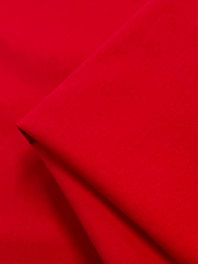 A close-up of Super Cheap Fabrics’ Plain Cotton - Watermelon (150cm) shows the neatly folded, lightweight fabric with a vibrant red hue and smooth texture.
