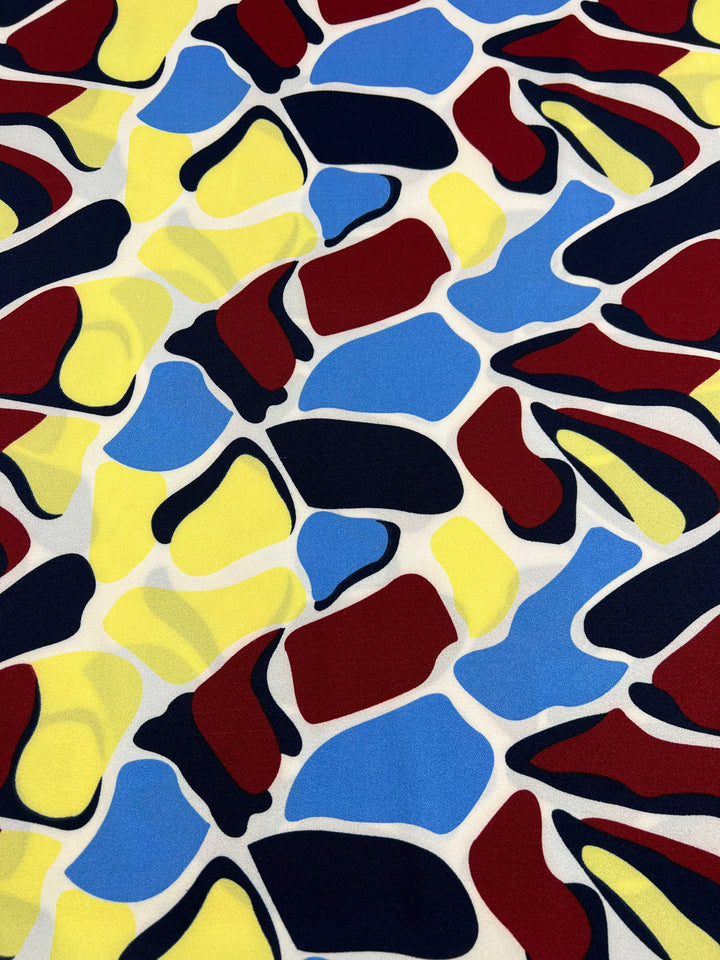 Bovine Rainbow Printed Crepe by Super Cheap Fabrics features overlapping red, yellow, blue, black, and white abstract shapes on lightweight 150cm polyester—ideal for bold, modern high-fashion and energetic styles.
