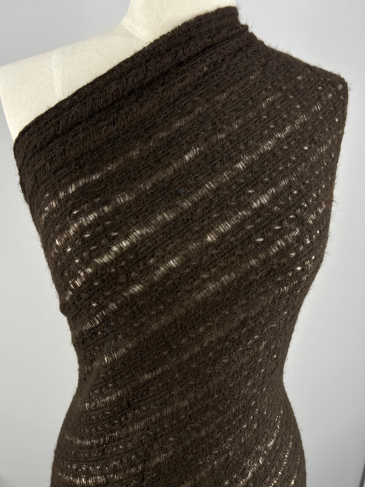 Super Cheap Fabrics' Wool Knit - Dark Chocolate (140cm) is a soft, semi-sheer, textured wool with an openwork pattern, draped diagonally over a white mannequin torso for a stylish, lightweight appearance.