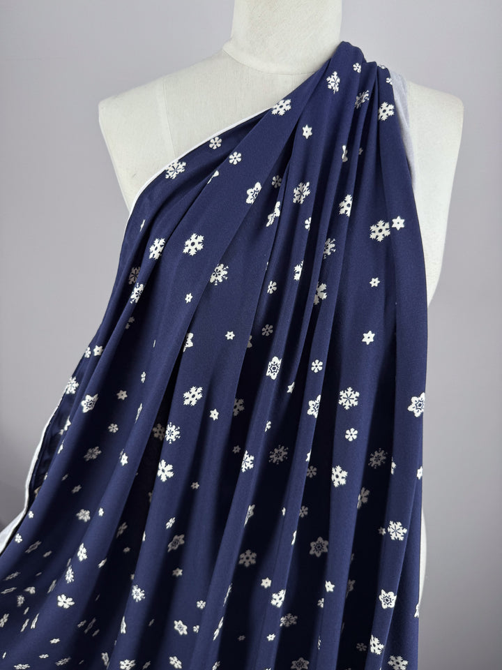 A mannequin is draped in Super Cheap Fabrics' Printed Cotton Lycra - Twinkle, 160cm wide, featuring navy white with small snowflake patterns, elegantly showcasing its smooth texture and design.