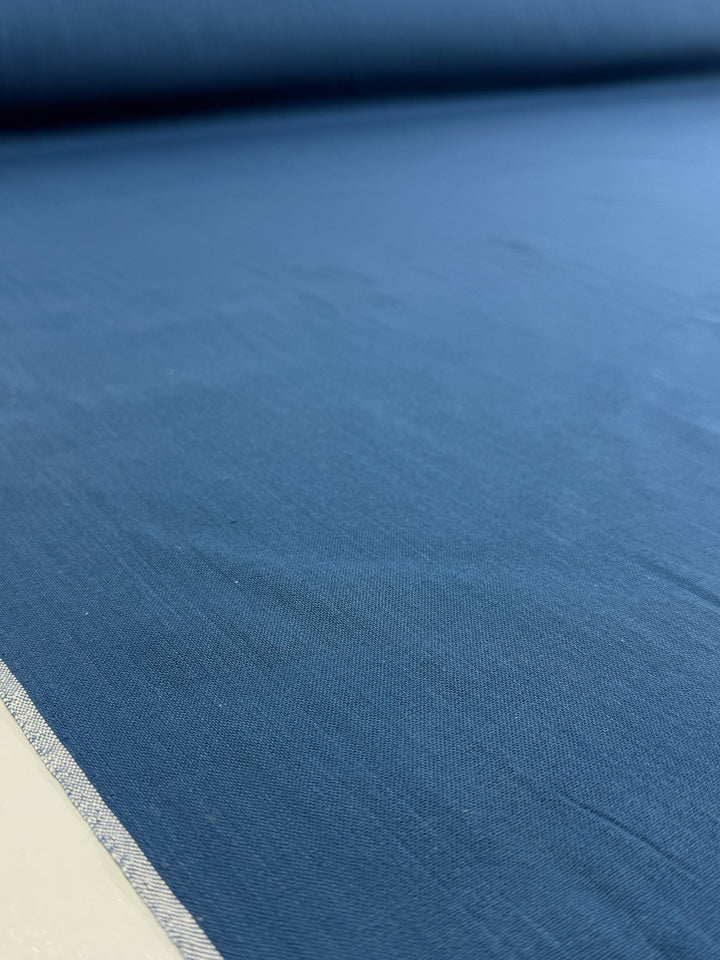 A close-up of Super Cheap Fabrics' Plain Cotton - Vallarta Blue - 108cm shows the texture and weave of the 100% cotton fabric, with a visible selvage edge on the left.