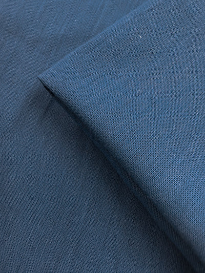 A close-up of two overlapping pieces of Super Cheap Fabrics' Plain Cotton - Vallarta Blue - 108cm shows fine threads, a subtle woven texture, and soft, smooth 100% cotton fabric with consistent color.
