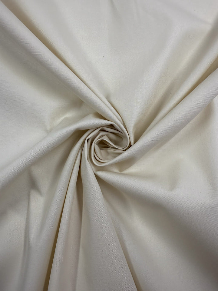 Super Cheap Fabrics’ Stretch Cotton in Antique White (147cm) is a lightweight fabric gathered and twisted into a central spiral, creating gentle folds and a smooth, elegant texture.