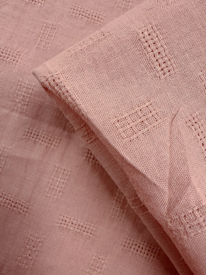 Close-up of Super Cheap Fabrics’ Textured Cotton - Misty Rose (140cm): lightweight cotton in light pink, showcasing a clear grid-like embroidered pattern with flat and folded sections for subtle geometric texture.