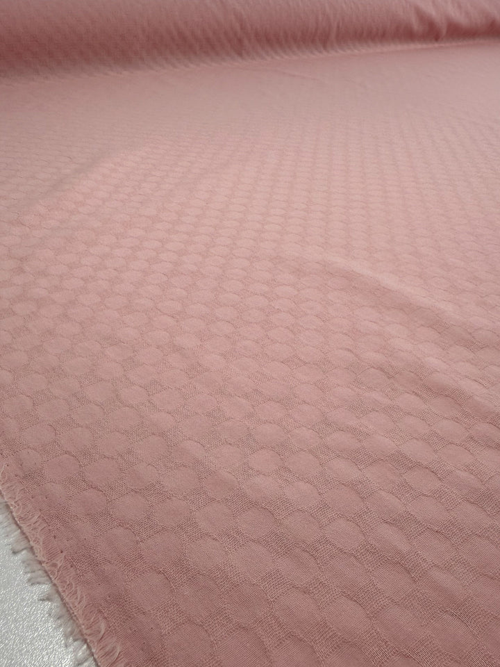 A close-up of Super Cheap Fabrics’ Textured Cotton - Chalk Pink (145cm) shows its circular pattern, smooth drape with a slight crease, and frayed edge—perfect for lightweight summer pants.