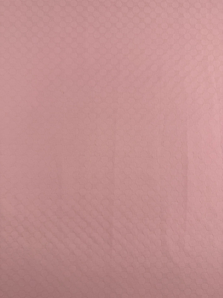 A close-up of Super Cheap Fabrics' Textured Cotton - Chalk Pink (145cm) reveals a lightweight fabric in light pink with a subtle hexagonal pattern, offering a delicate texture—perfect for summer cotton pants.