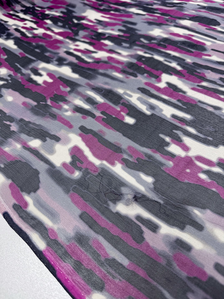 Detailed view of Super Cheap Fabrics' Pure Silk - Electric Mirage, showcasing an abstract, wavy pattern in purple, white, and gray. The design features dynamic, irregular overlapping shapes on a textured surface with elegant draping on a light background. Width: 132cm.