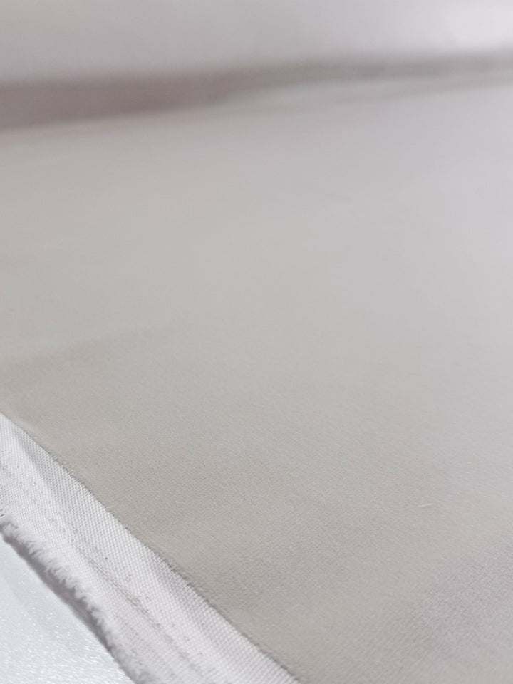 A close-up of Oxford Velvet - Warm Snow (144cm) by Super Cheap Fabrics, showing its smooth, light beige surface with a stitched edge in the lower left corner, lying flat.