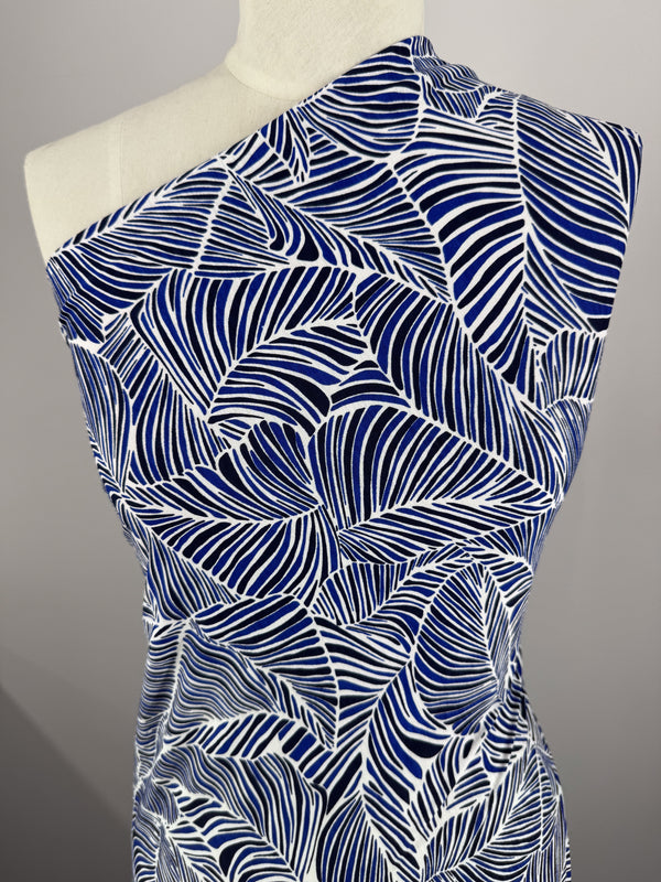 A mannequin is draped with Super Cheap Fabrics' Printed Lycra in Sapphire, featuring a bold blue and white abstract leaf design crafted from medium-weight Polyester/Spandex. Styled over one shoulder, it presents an elegant and modern look.
