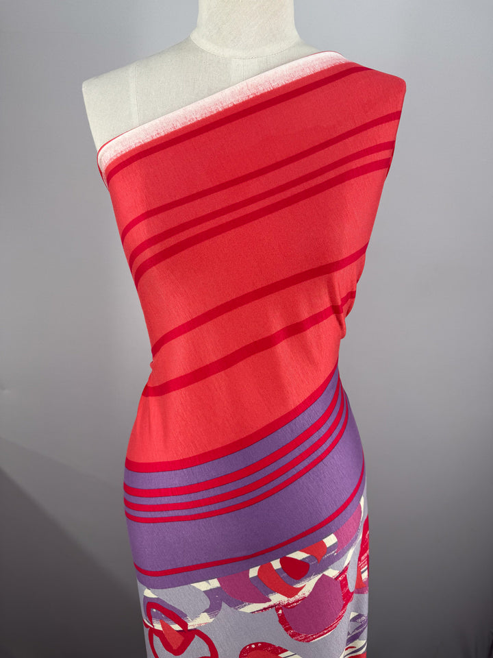 A mannequin is draped in Super Cheap Fabrics' Viscose Knit - Abstract Striped Geo (150cm), showcasing bold red and purple stripes on top with abstract red, purple, and white circular designs below.