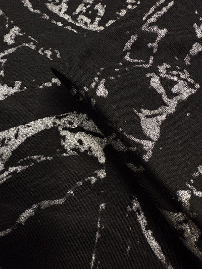 Close-up of Super Cheap Fabrics' Viscose Knit - Fossil (142cm) in black, featuring a silver abstract metallic pattern and modern medium-weight stretch texture, with gentle folds highlighting its striking design.