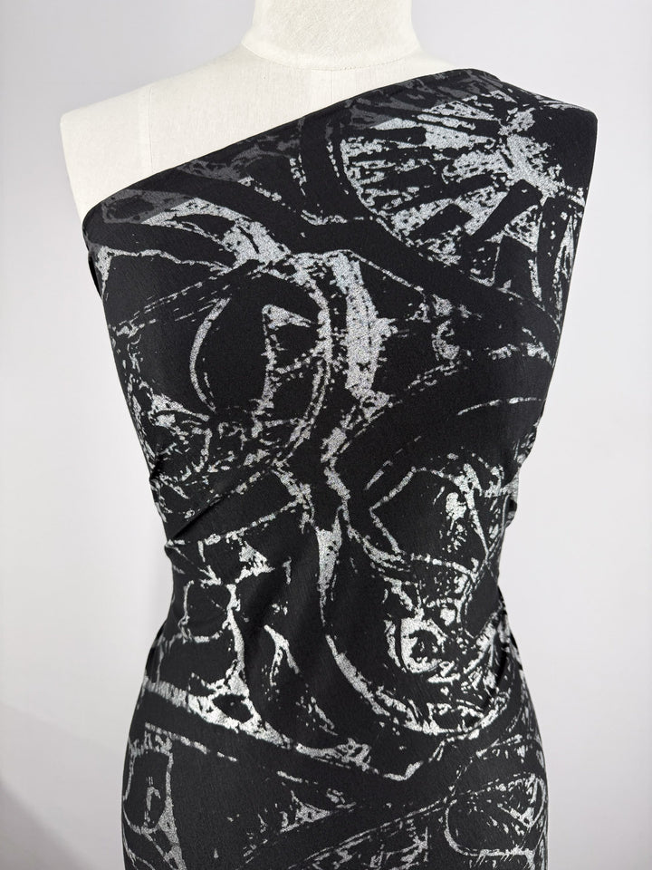 A black one-shoulder dress made from Super Cheap Fabrics’ Viscose Knit - Fossil (142cm), featuring an abstract silver pattern, is displayed on a mannequin against a plain, light background.