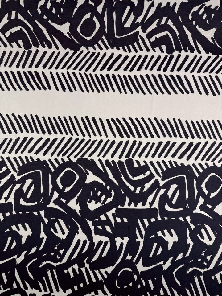 Super Cheap Fabrics’ Viscose Knit - Tribal Brushstroke (142cm) features abstract black shapes, parallel dashes, and bold organic patterns on beige—ideal inspiration for cool and breathable summer fabric designs.