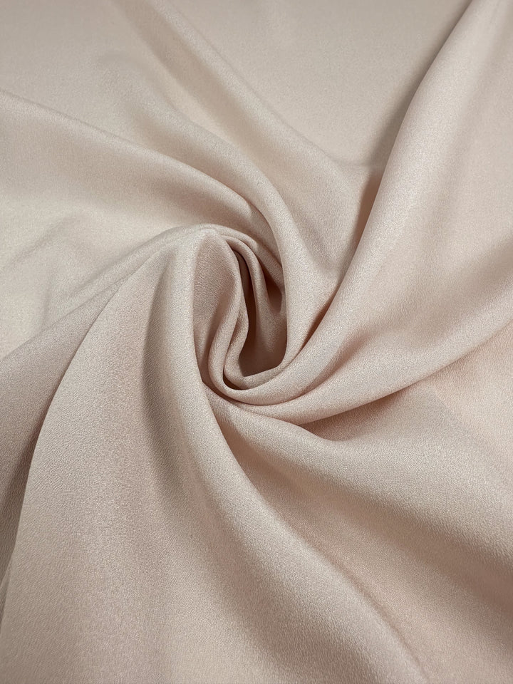 Close-up of Super Cheap Fabrics' Crepe - Mauve Chalk - 150cm fabric reveals a smooth, silky polyester texture with gentle twists and folds. Its lustrous and elegant drape, enhanced by a subtle sheen, highlights the beauty of this material.