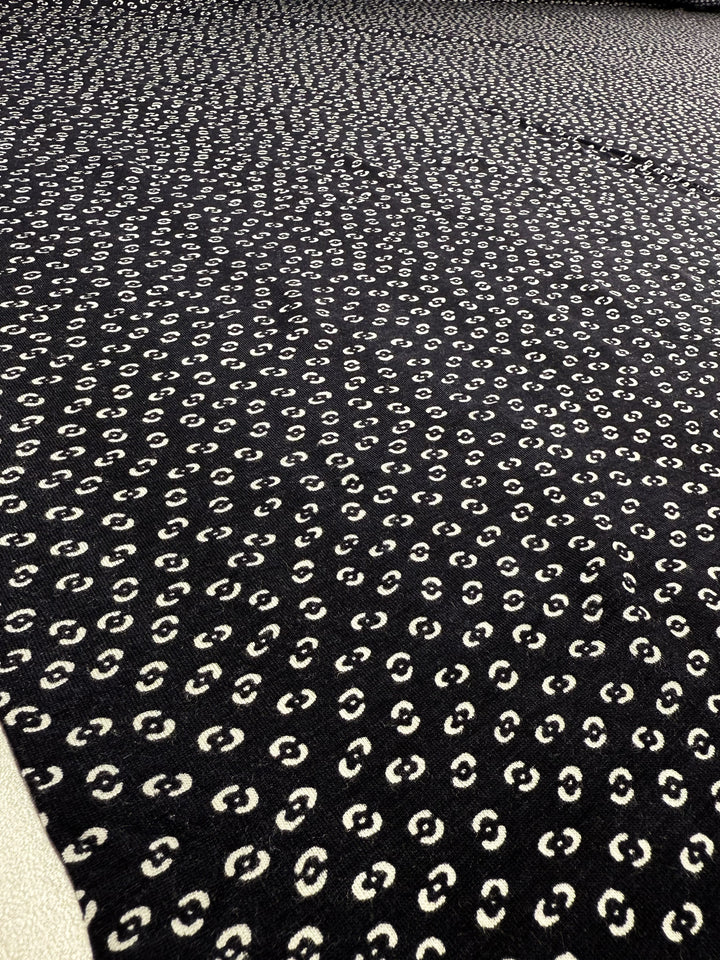 The Super Cheap Fabrics Viscose Knit - Micro Dot, 145cm wide, features a breathable dark fabric with a repeating pattern of small white dots that create a textured, dotted look—ideal for cool summer wear.
