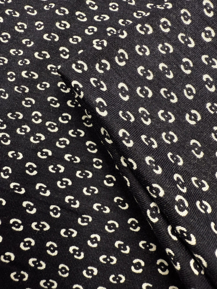 Close-up of Super Cheap Fabrics' Viscose Knit - Micro Dot (145cm), a black, medium-weight stretch fabric with a repeating pattern of small cream micro dots and a visible fold.