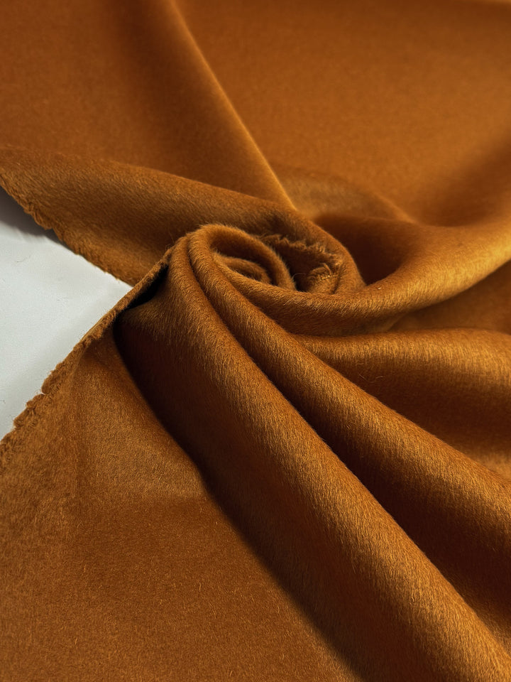 A close-up of Super Cheap Fabrics' Wool Cashmere in Roasted Pecan (150cm) highlights its soft, velvety texture, rich brown hue, loosely twisted center, smooth surface, and a slightly frayed edge on the left.