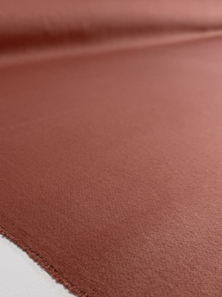 A close-up of Wool Cashmere - Canyon Clay (150cm) from Super Cheap Fabrics shows its smooth, reddish-brown, velvety texture. The luxurious fabric lies flat with gently curled edges, highlighting its premium quality and soft cashmere feel.