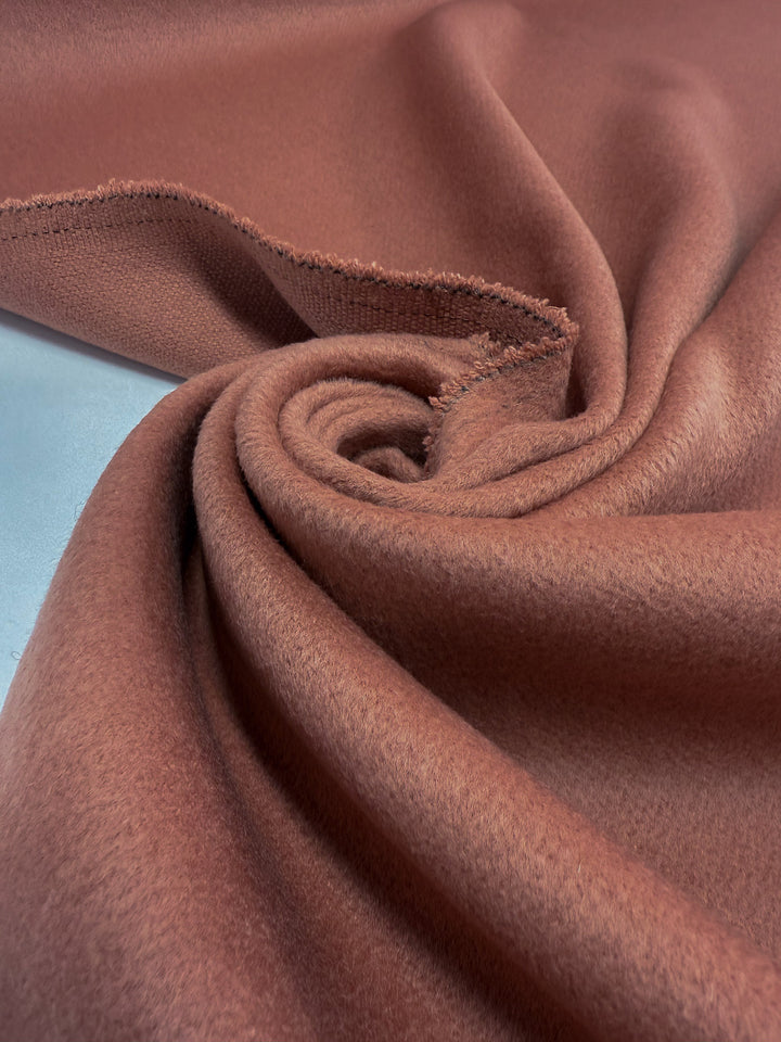 A close-up of Super Cheap Fabrics' Wool Cashmere in Canyon Clay (150cm), a soft, heavyweight material with a slightly fuzzy texture, artistically twisted into a spiral to reveal its raw edge.