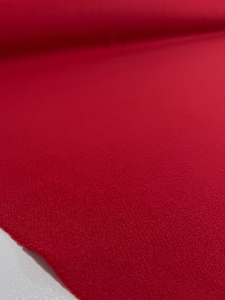 A close-up of Super Cheap Fabrics' Wool Cashmere in Cherry Red (150cm), an extra heavy weight, slightly textured fabric rolled out flat, displaying its thick, smooth surface and an unfinished edge in the foreground.