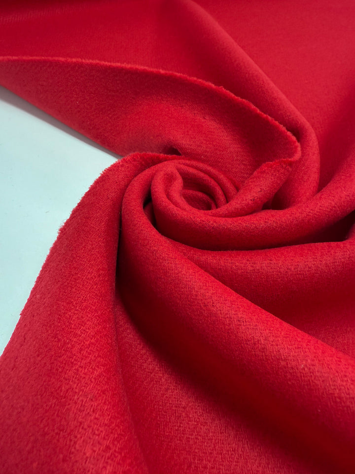 Super Cheap Fabrics' Wool Cashmere - Cherry Red - 150cm is displayed in a swirl, highlighting its soft texture and smooth folds in a vibrant cherry red shade.