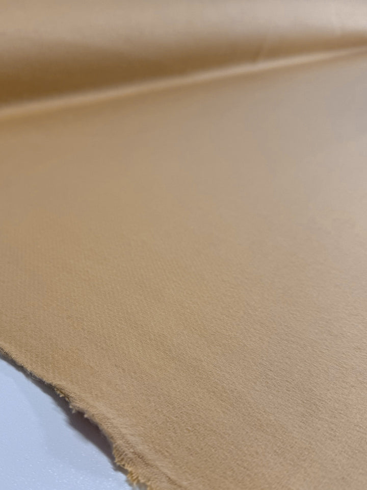 A close-up of Super Cheap Fabrics' Wool Cashmere - Sahara Sun (150cm) in light brown, showing its extra heavy weight, luxurious softness, subtly textured surface, and a raw edge laid flat on a smooth background.