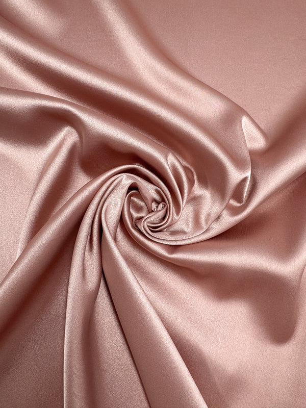 Satin Deluxe - Terra Cotta by Super Cheap Fabrics features smooth, shiny rose gold satin (150cm wide) with soft swirling folds and a glossy finish for an elegant, luxurious texture.