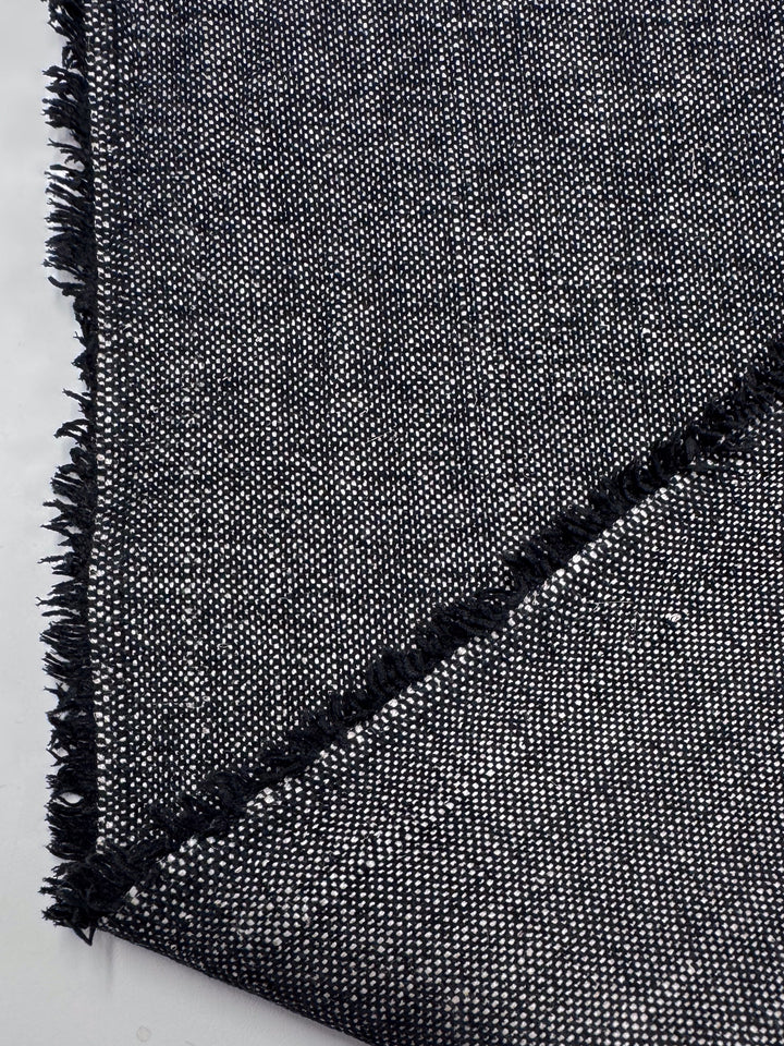 Close-up of Upholstery Tweed - Dresden Charcoal (146cm) by Super Cheap Fabrics, showing its black and white woven surface with diagonal fold, fringed edge, and speckled texture—ideal for upholstery from this Australian wholesaler.