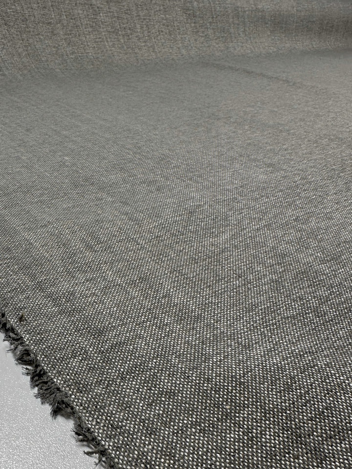 The Upholstery Basket Weave - Dresden Warm Silver from Super Cheap Fabrics features a textured gray fabric with a slightly frayed edge, showcasing a structured weave pattern. This medium-weight fabric is 145cm wide and elegantly covers the entire image.