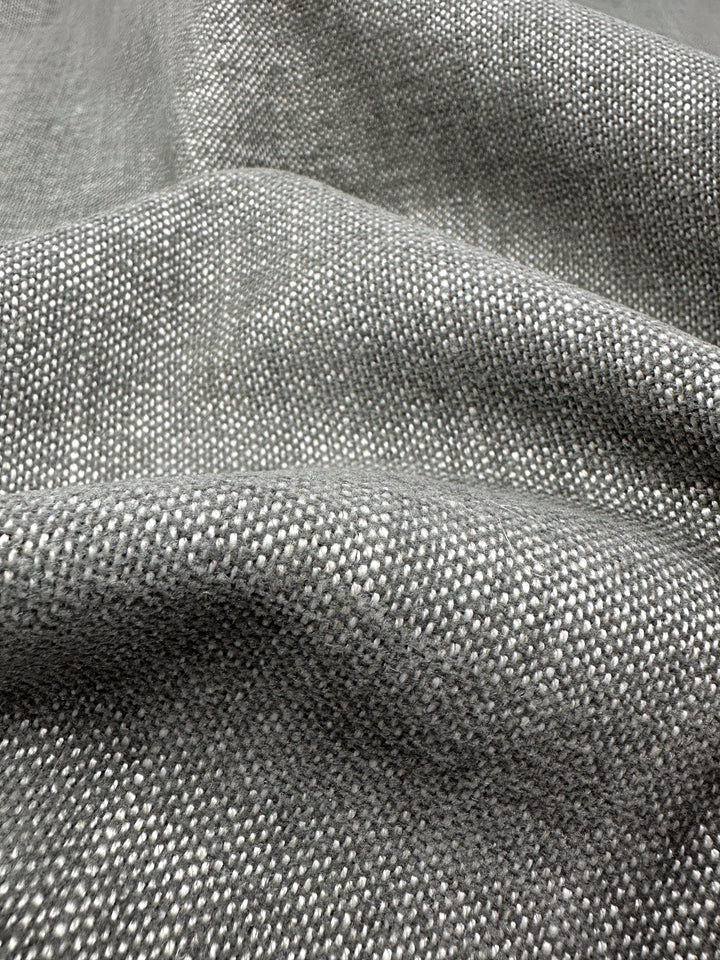 The medium-weight "Upholstery Basket Weave - Dresden Warm Silver - 145cm" by Super Cheap Fabrics features a gray, textured surface with a subtle grid pattern. Its soft and gracefully foldable material highlights the intricate weave and structured texture.