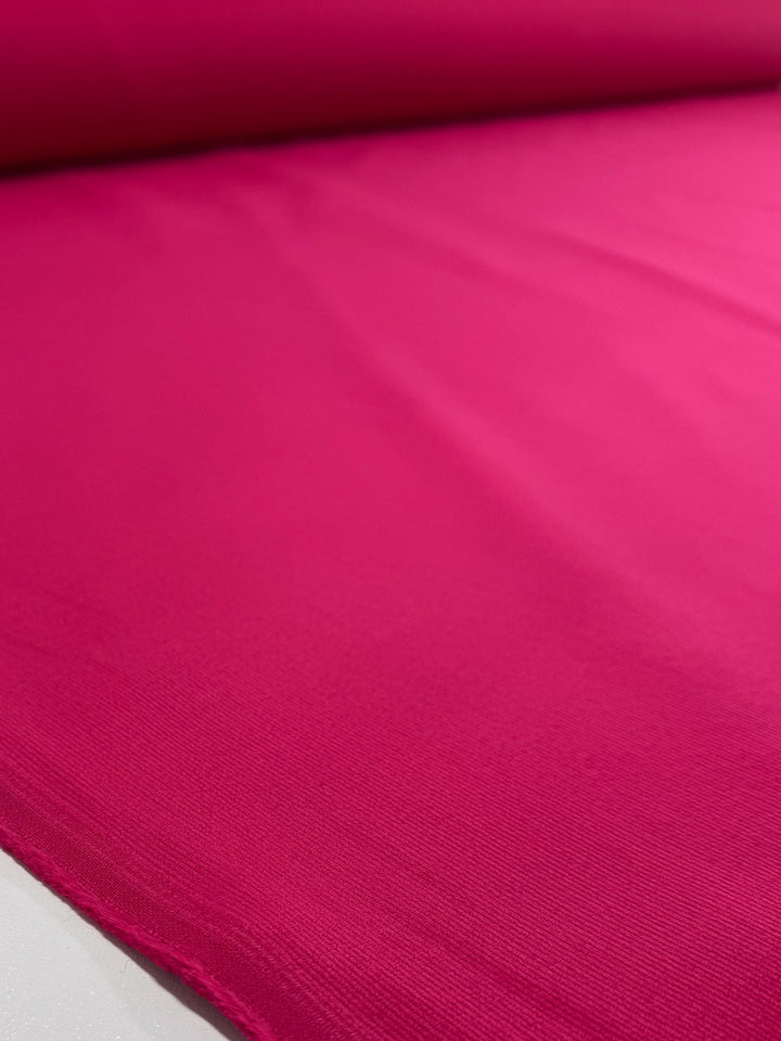 A close-up of Super Cheap Fabrics' Pin Wale Corduroy - Love Potion (147cm) unrolled, displaying its smooth texture and vibrant pink color.