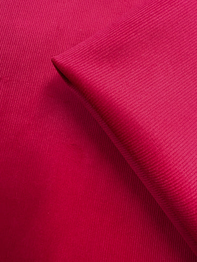 A close-up of Super Cheap Fabrics’ Pin Wale Corduroy - Love Potion (147cm), showing its bright pink color, fine ribbed texture, and smooth, medium weight cotton fabric with a neatly folded corner.